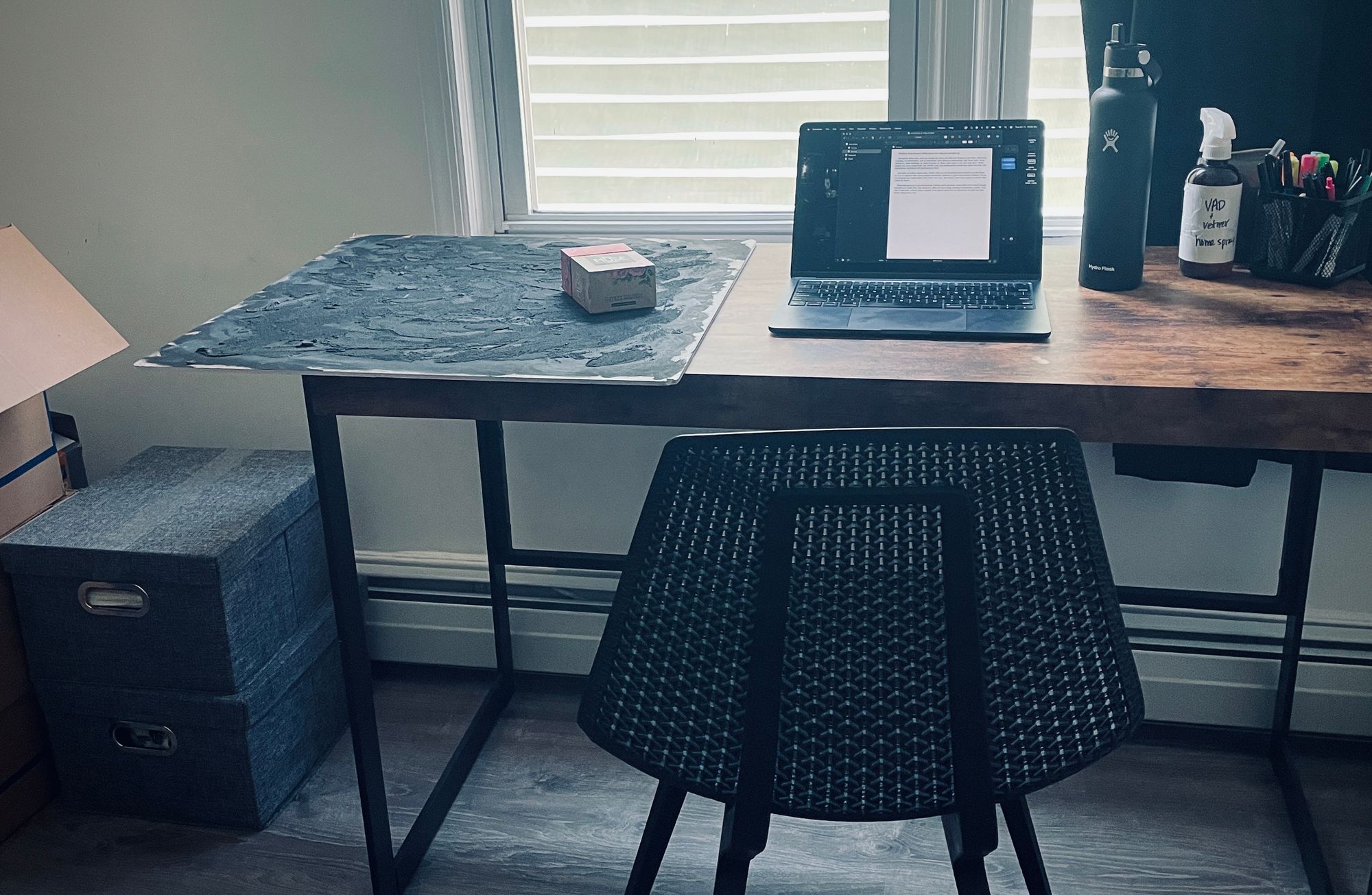 photo of a wooden desk and black chair, with a laptop, deck of tarot cards, and writing materials.