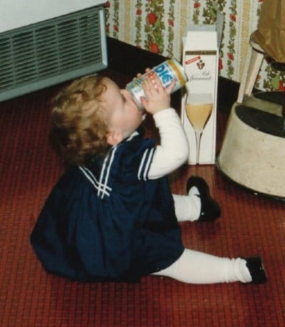 meg as a baby, sitting on the floor in a blue and white dress, attempting to drink a can of soda from the wrong end