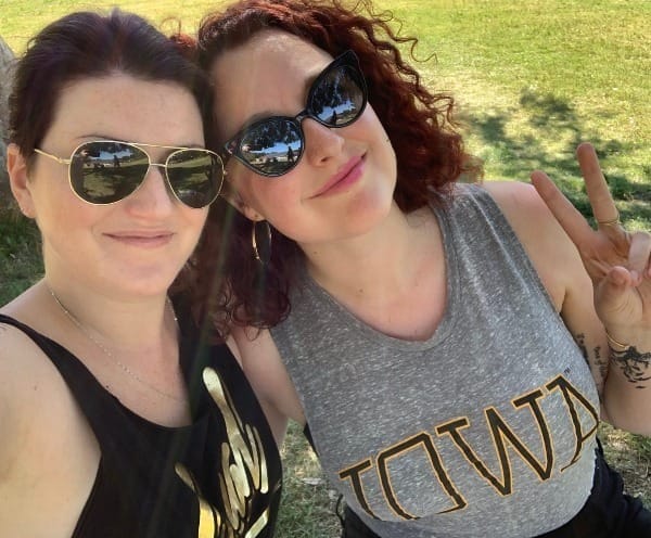 meg & jeanna in sunglasses, smiling at the camera with grass in the background