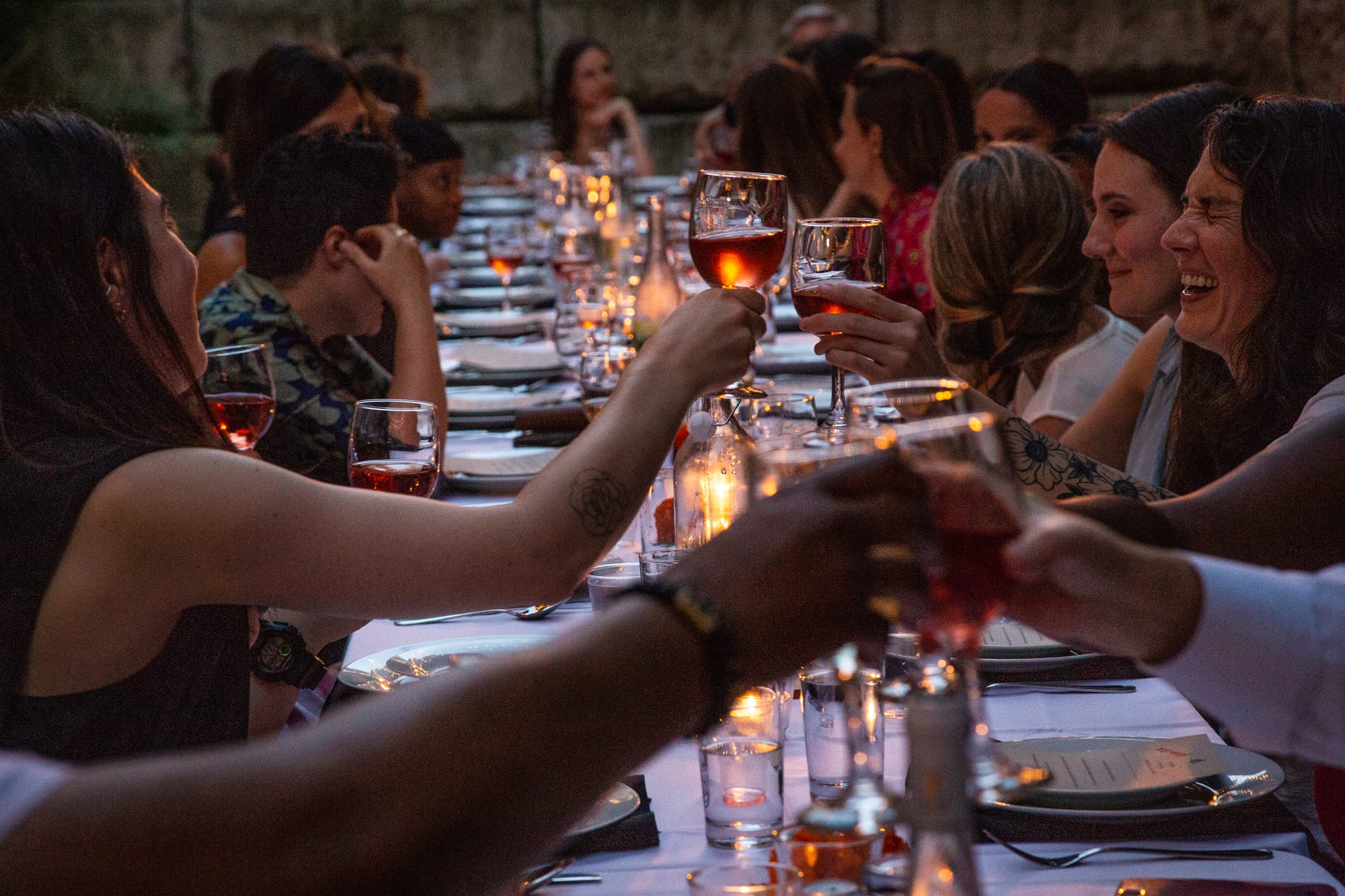 long dinner table filled with laughing, smiling people of many genders and races, toasting wine glasses