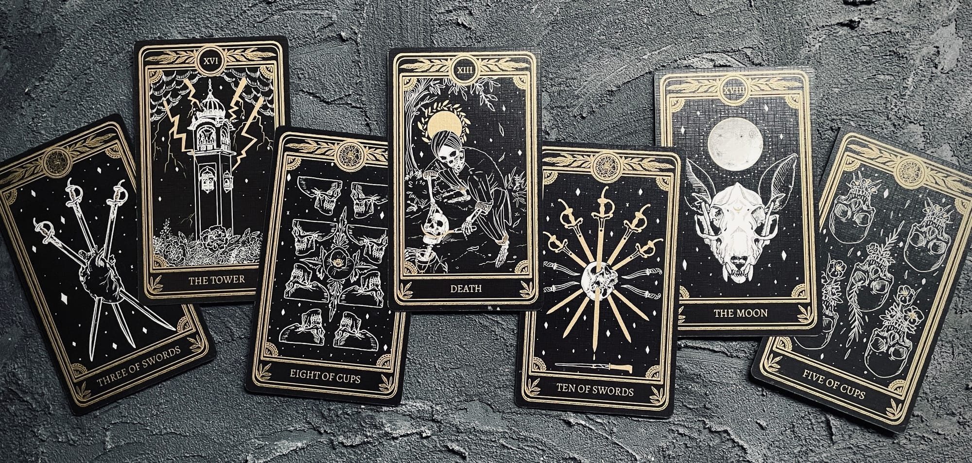 from left to right, cards from the marigold tarot: three of swords, tower, eight of cups, death, ten of swords, moon, five of cups