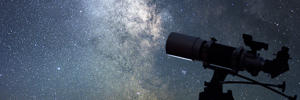 telescope in the foreground, with a dark sky full of stars in the background