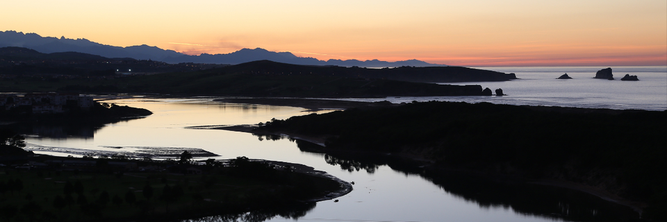 image of an estuary: fresh water river flowing into the sea, surrounded by dark ground with mountains and sky behind